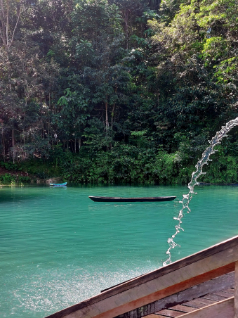 Lago de cor azul, com canoa e fundo cheio de árvores.